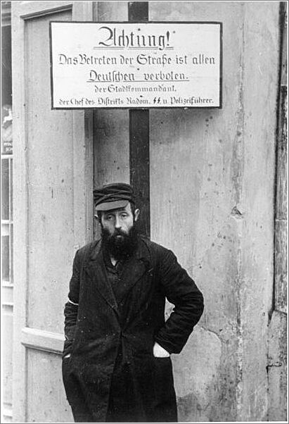 A Jew forced to stand below a German warning sign in Radom
